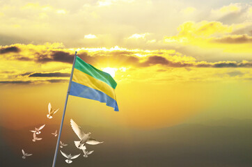 Gabon flag waving with flying doves against sunset or sunrise. Gabon flag for Republic Day and Independence Day.
