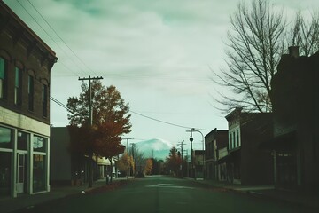 Deserted small town main street with distant snow-capped mountains, partly cloudy sky, past liveliness signs, and autumn colors.