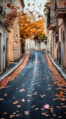 Obraz premium A serene autumn street lined with colorful fallen leaves and charming buildings.