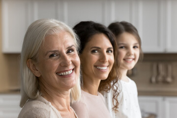 Three generations of women portrait, close up focus on happy grandmother, her grownup daughter and granddaughter on background. Different stage of life, family unity, heritage, generational connection