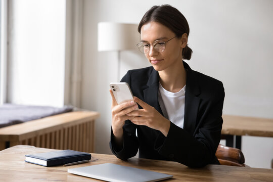 Attractive businesslady sit at workplace desk with smartphone, using mobile banking or financial management tools, planning, organizing workday, solve work-related matters efficiently via application
