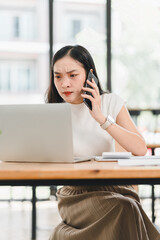 Focused woman on phone, working on laptop in modern office space, showing determination and...