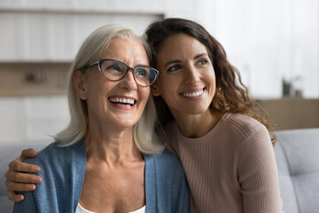 Dreamy pensive young woman hugging older mother smile looking away, feel happy, enjoy priceless and...