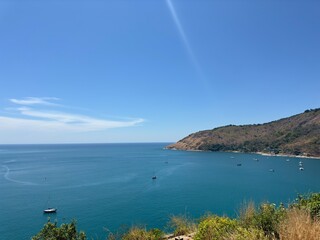 Obraz premium Breathtaking coastal view of a tranquil bay with boats near a hilly shoreline under a clear blue sky