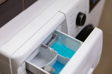 A detailed closeup view of a washing machines detergent drawer filled with blue liquid detergent