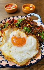 Close up Thai fried egg with spicy stir fried braised beef tendon basil in dish on wooden background and blurred sauce. Special meal and Famous food in Thailand. Selective focus.