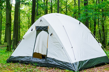 Tent in the forest in white and green. Nature travel outdoor concept. A large tent stands on the edge of a green forest. A large tent stands on the edge of a green lifestyle forest.