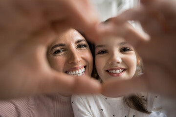 Beautiful mother and little adorable daughter showing symbol of love with joined fingers, laughing,...