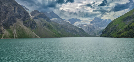Kaprun high mountain reservoirs - impressive dramatic sky. Bad weather in summer - dark blue, grey sky over the grey, green mountains. August 20, 2024.