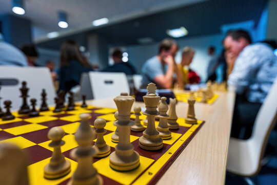 Dynamic chess tournament scene with wooden chess pieces on a vibrant yellow board, players deeply engaged in strategy and mental skill, emphasizing precision and focus.