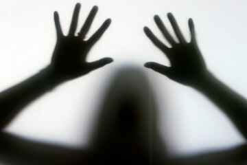 Silhouette of a woman behind the glass. Woman showing gesture stop. Stop violence and sexual abuse against women. Melancholy and crisis concept.