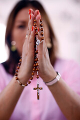 Catholic woman praying with a silver crucifix and a rosary with beads.