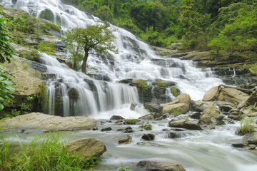 Obraz premium stunning waterfall cascades over rocky terrain, surrounded by lush greenery and trees, creating serene natural landscape. flowing water adds sense of tranquility and beauty to scene