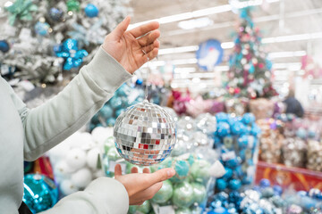 Woman's hand holding decorative silver disco ball over the xmas store background, Christmas tree toy decorations, shopping for a classic holiday home decor, preparation for winter holidays, free space