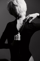 Stylish woman with short hair zipping up black bodysuit, conveying elegance and confidence. Black...
