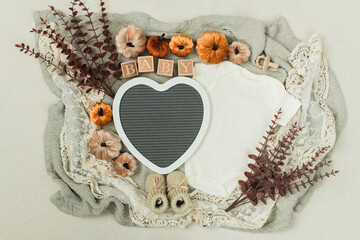 A cozy flat lay featuring a baby bodysuit, pumpkins, leaves, and rustic fall decor. Perfect for...