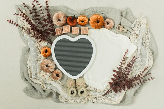 A cozy flat lay featuring a baby bodysuit, pumpkins, leaves, and rustic fall decor. Perfect for pregnancy announcements, autumn themes, and family designs.