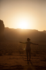 Fototapeta premium silhouette of a young beautiful girl scattering sand from her hands in the wind while being in desert during the sunset