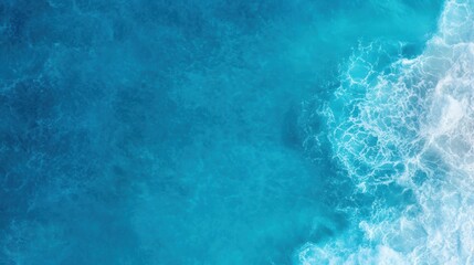 Fototapeta premium A vibrant aerial view of the ocean, showcasing its clear blue waters and frothy white waves, This image can be ideal for travel blogs, beach resort advertisements, or environmental campaigns,