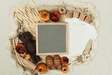 A cozy flat lay featuring a baby bodysuit, pumpkins, leaves, and rustic fall decor. Perfect for pregnancy announcements, autumn themes, and family designs.