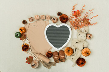 A cozy flat lay featuring a baby bodysuit, pumpkins, leaves, and rustic fall decor. Perfect for...