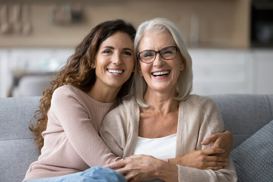 Portrait of two beautiful young and mature females, different generations women hugging sit on sofa, sharing warmth, joyful moments together. Family ties, intergenerational connection, love, support