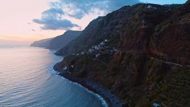 Houses and gardens located on the sloping mountain. Rocky coast of Madeira, Portugal at sunset.
