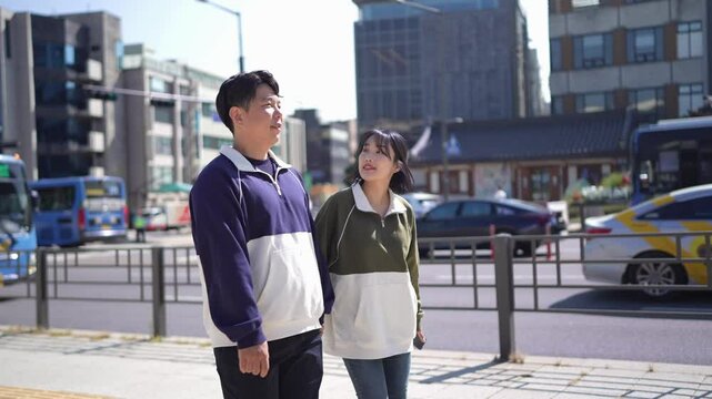 A young couple wearing tracksuits strolls through the streets of Seoul, South Korea in the fall of October 2024. Slow motion video.
