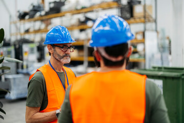 Engineers wearing safety vests and helmets discussing in factory