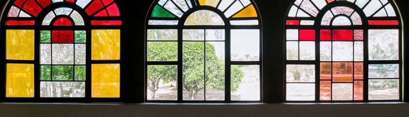 Colorful stained glass windows framing a view of greenery outside.