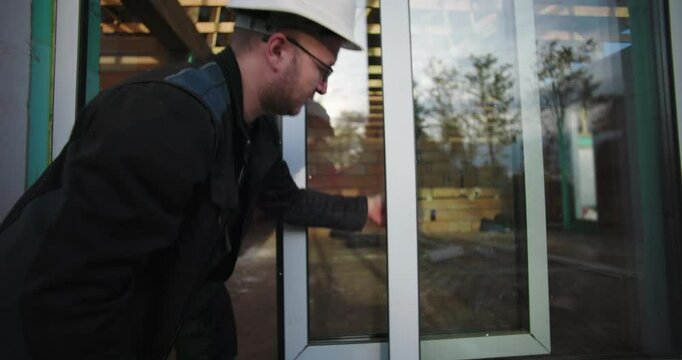 Worker checks window alignment on construction site, focused on installation quality and frame adjustment for residential project