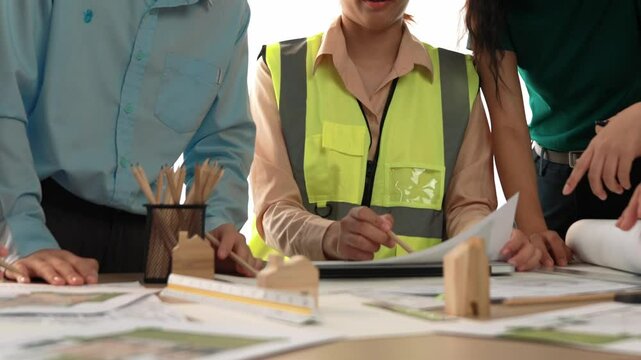 Smart architect and safety engineer discussion about building blueprint on table with architectural document, measurement tools and wooden block scatter around at modern office. Closeup. Delineation.
