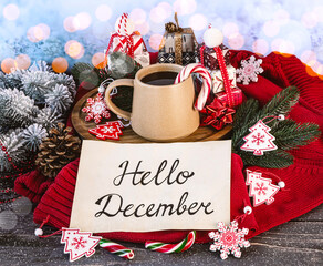 Hello December concept. Beige cup of coffee, Christmas decorations, gift boxes, lollipops, warm sweater, fir branches on snowy background.