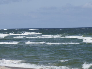 Waves crashing on the shore under a clear sky, creating white foam