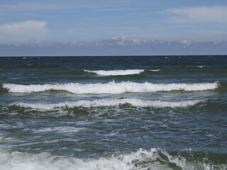 Waves on the sea under a blue sky with white clouds and horizon on a summer day