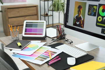 Designer's workplace with computer, tablet, color palettes and stationery on wooden table indoors