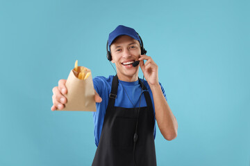 Fast-food worker with fries in paper bag on light blue background, selective focus