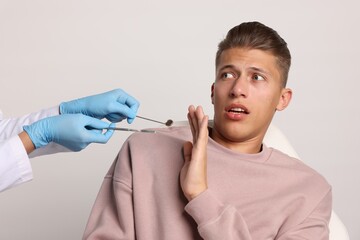 Dental phobia. Dentist working with scared man on light grey background, closeup
