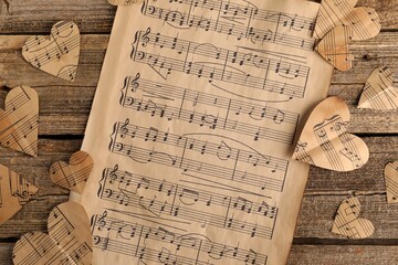 Paper hearts with notes and musical note sheet on wooden table, flat lay