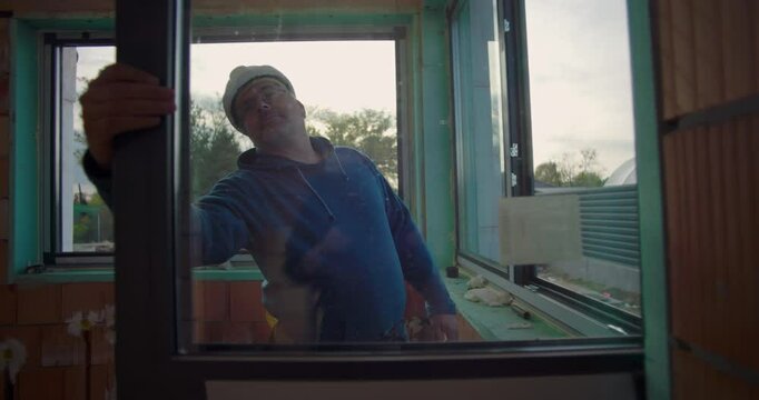 Worker on construction site verifying window installation in residential building project, focused on alignment and fit