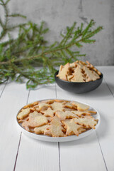 Homemade shortbread cookies with sugar in a white plate on the foreground and in a deep black one on the back. A large branch of a fir tree at the back. Vertical location.
