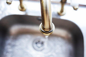 Gold running tap with water falling into silver metal sink 