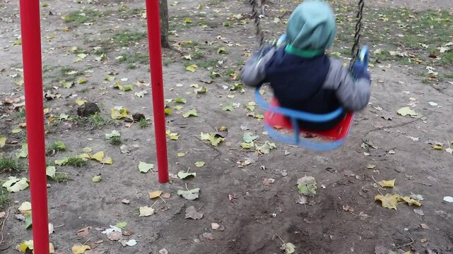 A little boy rides on an old swing on the playground
