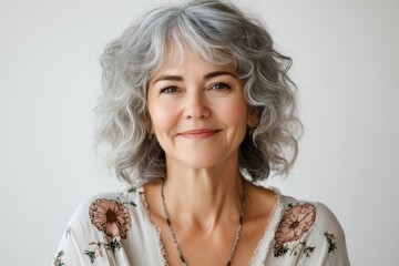 A woman with a silver haired head and a necklace with a flower design. She is smiling and looking at the camera