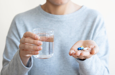 Person holding pills and glass on white background