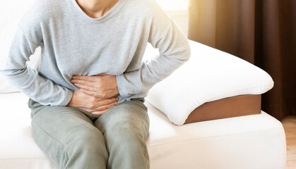 Young woman sitting on a sofa, holding her belly with a painful expression