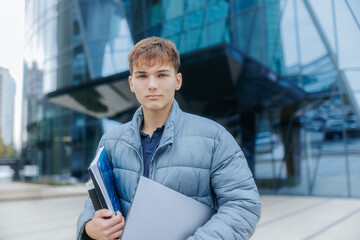 Young male student outdoors, carrying books and laptop on campus