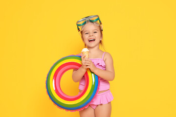 Cute little girl in swimsuit with inflatable ring eating ice cream on orange background