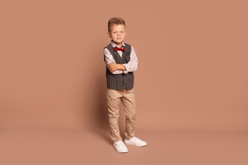 Full length portrait of little boy with stylish clothes on brown background