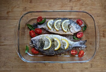 Fresh dorado fish prepared with lemon slices, cherry tomatoes, and herbs, ready for baking in dish